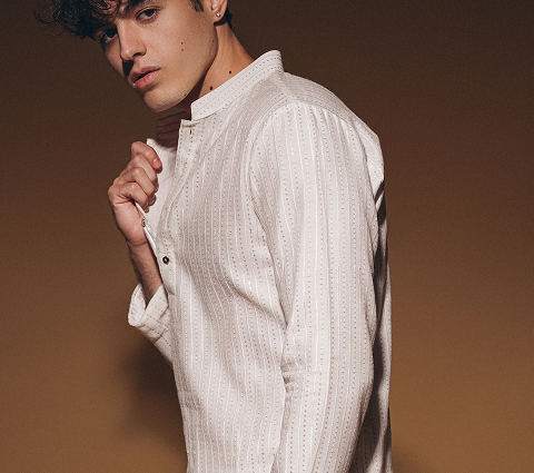 Young man poses in a textured white kurta against a warm brown background