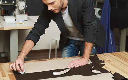 Man traces a clothing pattern onto fabric on a wooden table