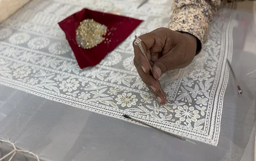 Person embroidering silver floral patterns on fabric