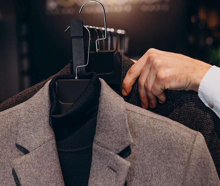 A hand holds a hanger with a gray blazer